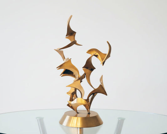 Abstract bronze sculpture on an oval glass coffee table top in a contemporary minimalist living room with curved walls and overhead lighting with curved walls 